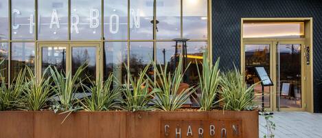 A building with a large glass facade displaying the name 'CHARBON' and a metal planter with the same name.