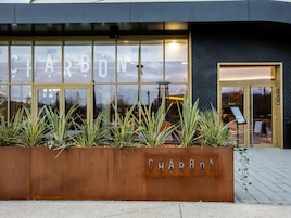 Un edificio con un amplio frente de vidrio que muestra el nombre 'CHARBON' y una jardinera metálica con el mismo nombre.