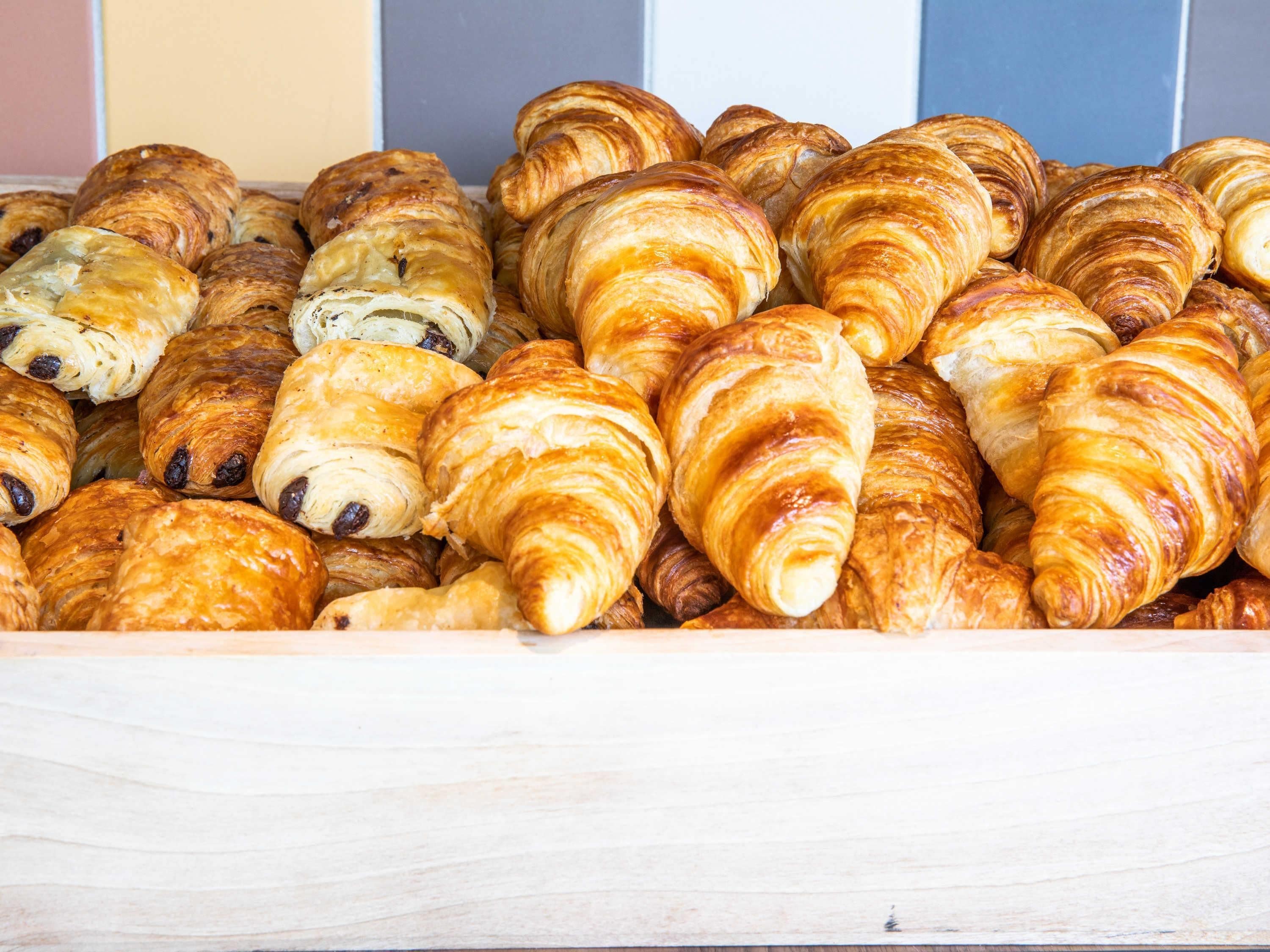 A variety of pastries, including croissants and chocolate rolls, displayed in a wooden container.
