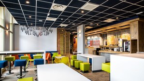 Ein modernes Café mit bunten Sitzgelegenheiten, einer Bar und einer gut sichtbaren Speisekarte.