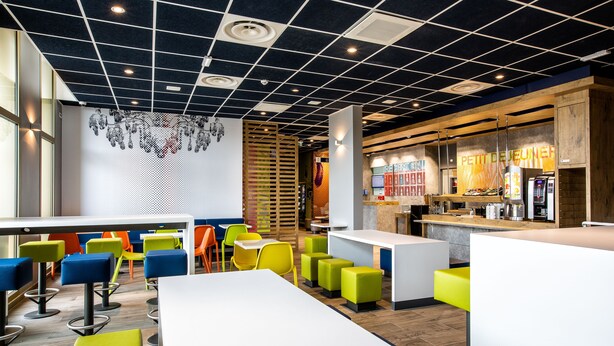 Un café moderne avec des sièges aux couleurs vives, un coin bar et un tableau des menus bien visible.