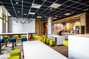 Un café moderne avec des sièges aux couleurs vives, un coin bar et un tableau des menus bien visible.