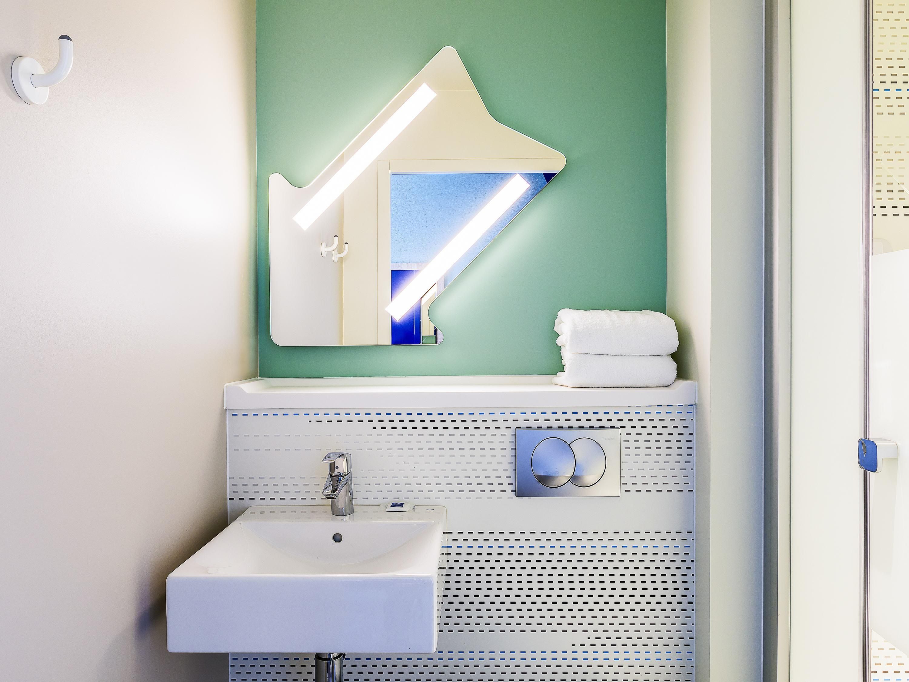 Een badkamer met een wit wastafelmeubel, een spiegel met een bijzondere vorm en een handdoekrek.