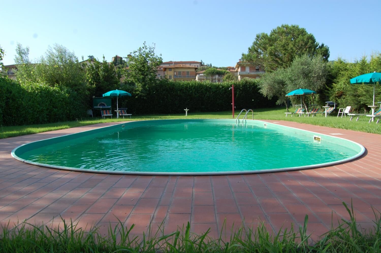 Una piscina con plataforma de baldosas, rodeada de vegetación y algunas sillas de descanso.