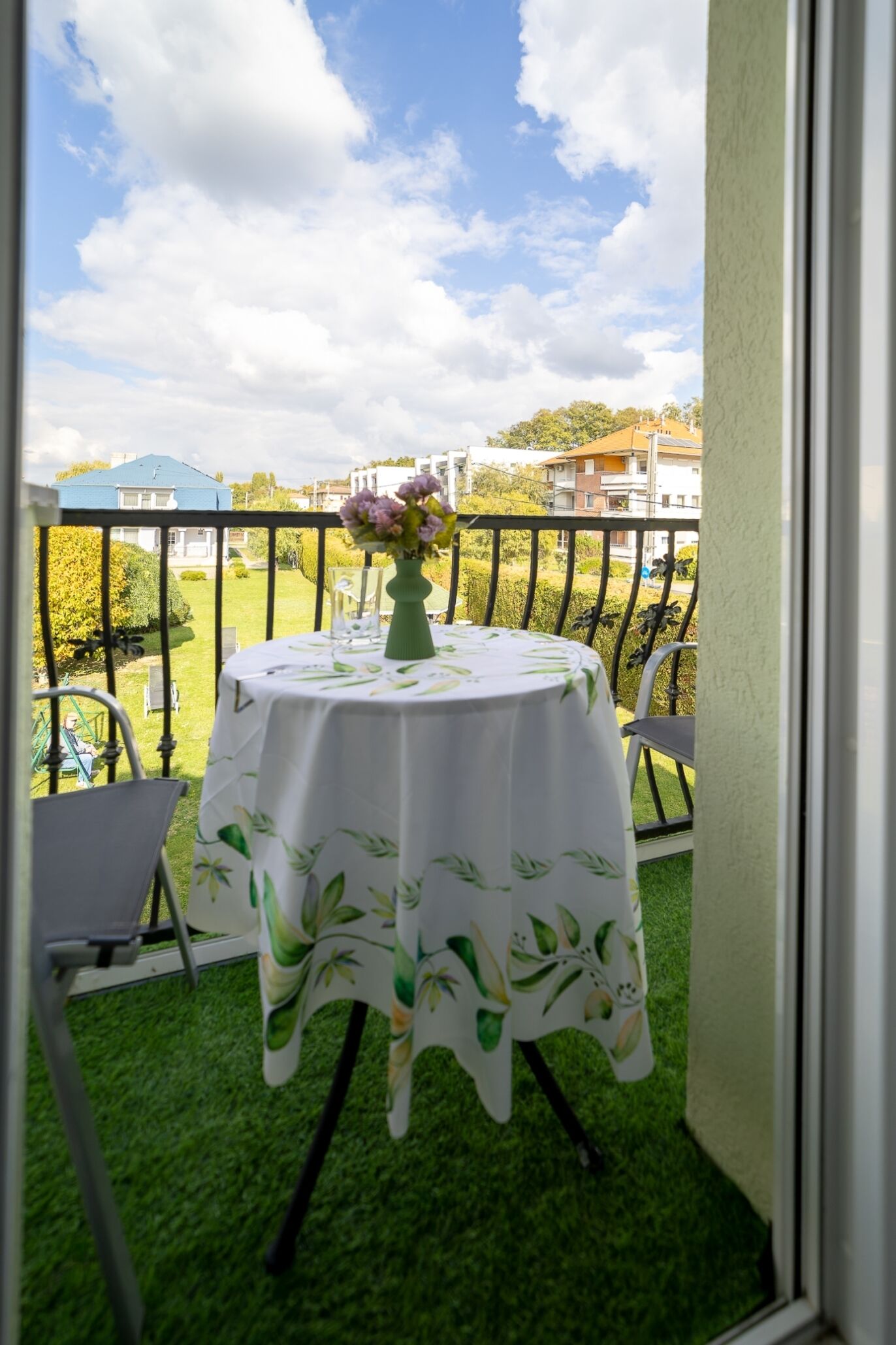 A balcony with a round table, chairs, and a vase of flowers.