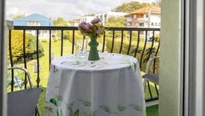 A balcony with a round table, chairs, and a vase of flowers.