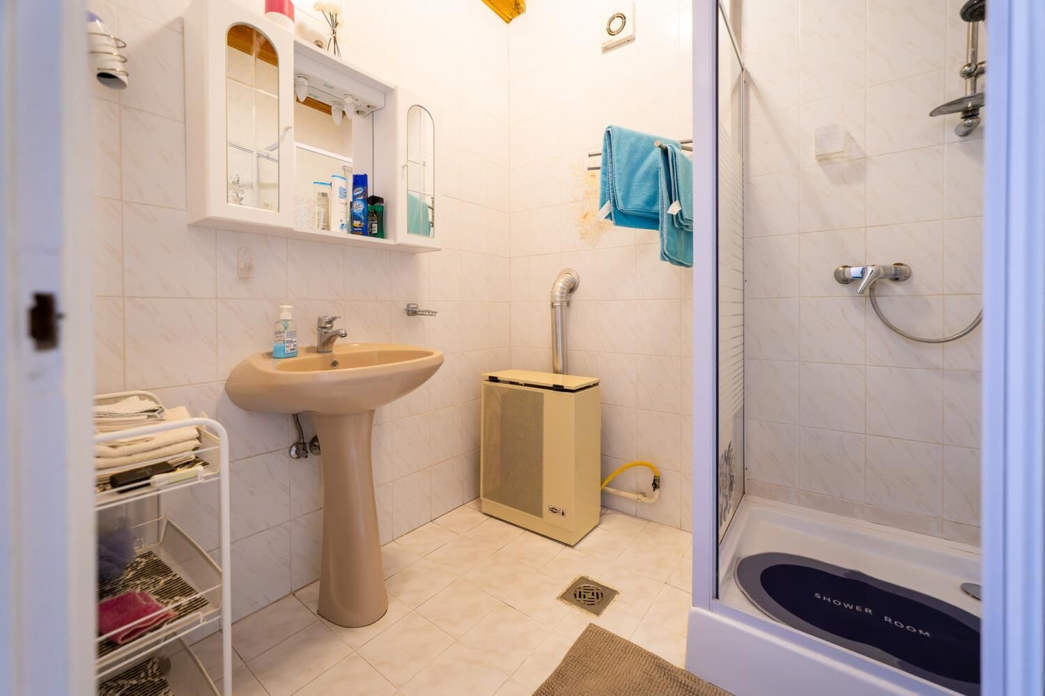 Un bagno con lavandino, specchio, asciugamano, doccia e un piccolo armadietto.