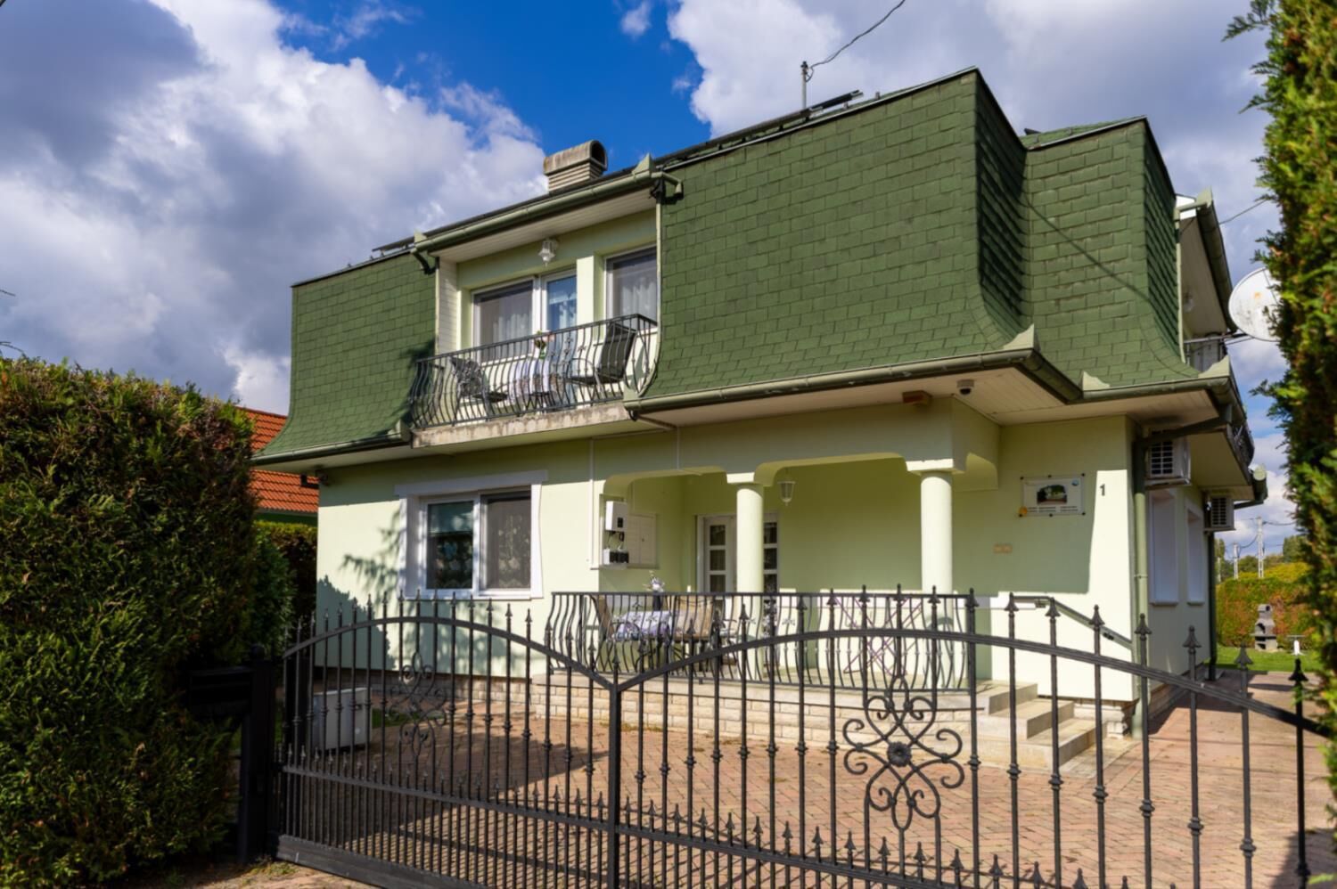 Un edificio de dos pisos con techo verde, un balcón en el nivel superior y una entrada con reja.