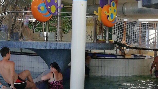 An indoor water play area with colorful butterfly-shaped water features and a pool with people around.