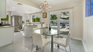 Een moderne keuken met een glazen eettafel, witte stoelen en een roestvrijstalen koelkast.