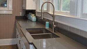 A kitchen with a stainless steel sink, white cabinets, a window with white curtains, and a patterned rug. - Starfish House Savannah Fort Stewart GA (Richmond Hill)