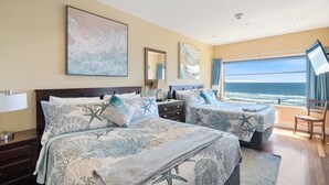 A hotel room with two beds, a large window with a view of the ocean, and artwork on the walls. - Three Arch Inn (Tillamook)