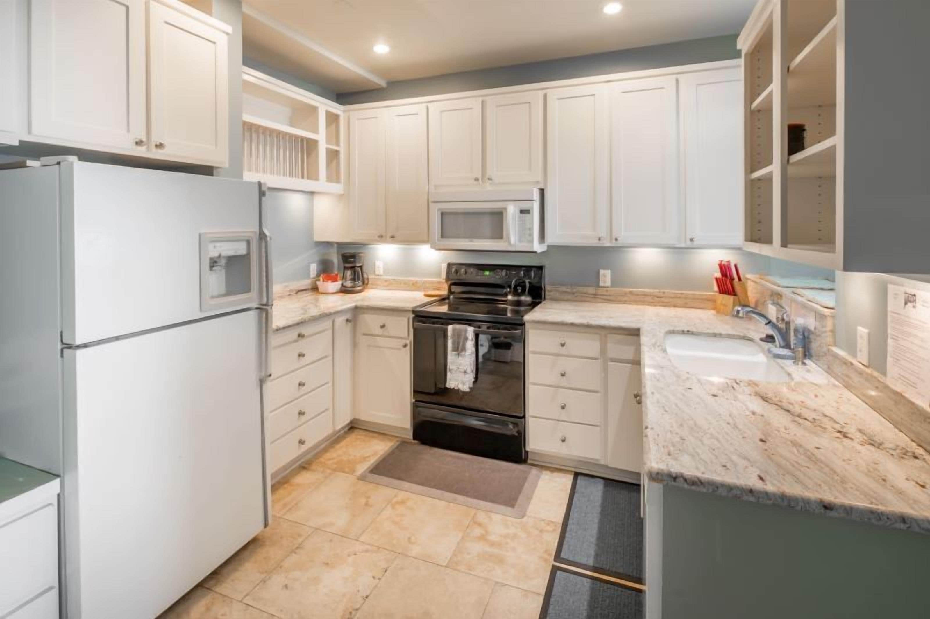 A modern kitchen with white cabinets, a built-in microwave, a stove, and a sink.