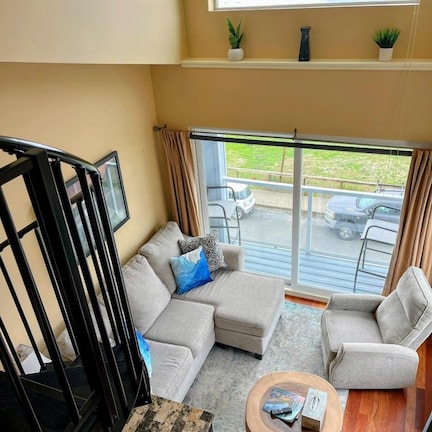 A spacious living area with a large window overlooking the ocean, a sofa set, a coffee table, and a staircase.
