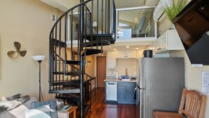 A compact kitchen with a built-in stove, a refrigerator, and a dining area with a wooden bench and a sofa. - Three Arch Inn (Tillamook)