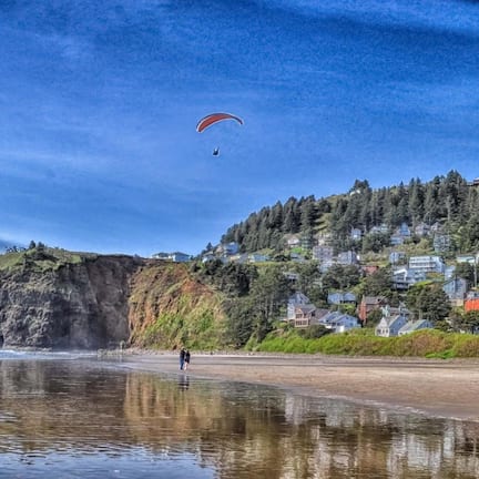 A coastal scene with a beach, cliffs, and a hillside with houses.