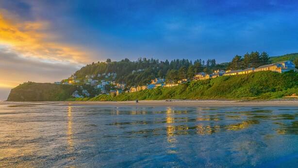 A coastal landscape with a beach, houses on a hillside, and a sunset. - Three Arch Inn (Tillamook)
