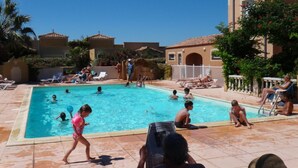 A swimming pool area with multiple pools, lounge chairs, and a building with a tiled roof.