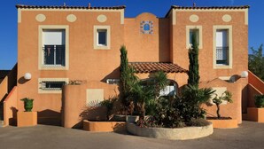 A building with a stucco exterior, a tiled roof, and a central courtyard with plants.