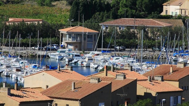 A marina with multiple boats docked, surrounded by buildings with red-tiled roofs.
