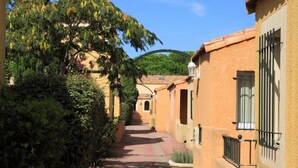 A narrow alleyway with buildings on either side, a tree-lined path, and a clear blue sky.