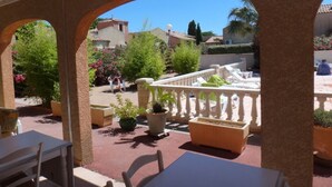 An outdoor patio area with tables and chairs, surrounded by arches and potted plants.