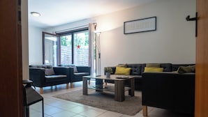 Een moderne woonkamer met een bank, fauteuils, een salontafel en een open haard.