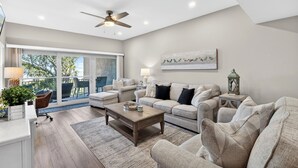 A modern living room with a ceiling fan, a large window with a view, a fireplace, and a dining area. - 463 Captains Walk is a gorgeous villa with breathtaking views of the ocean. (Hilton Head)