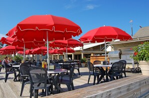 Mesas y sillas al aire libre con sombrillas rojas, una parrilla de barbacoa y una terraza de madera.