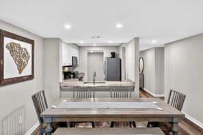 Un comedor moderno con una mesa de madera, sillas y una cocina al fondo.