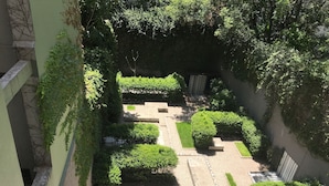 Une cour intérieure avec une zone centrale pavée, entourée de verdure et de jardinières en pierre.