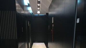 Un couloir doté d’un sol carrelé, de murs sombres et d’un panneau rouge indiquant la sortie de secours.