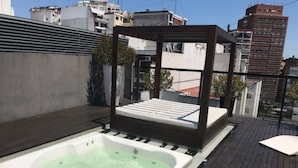 Un bain à remous sur une terrasse en bois, surmonté d’une structure métallique.