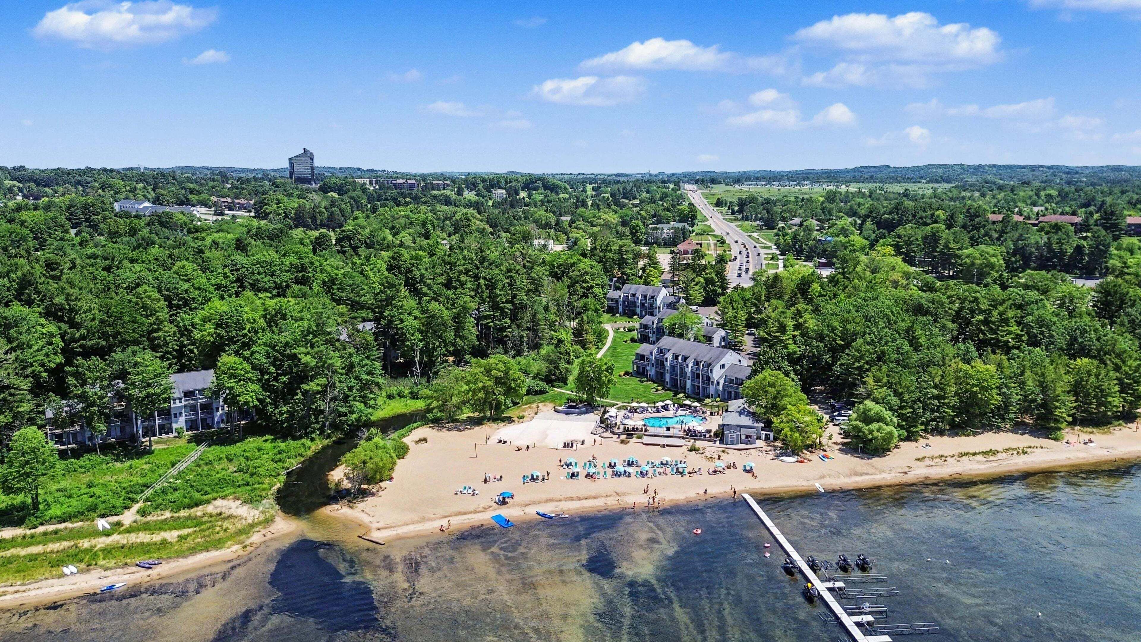 An aerial view of a coastal resort with a swimming pool, beach, and dock.