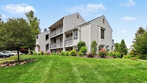 A multi-story residential building with balconies, a well-maintained lawn, and surrounding greenery.