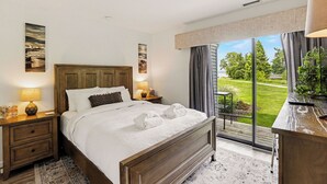 A hotel room with a large bed, two bedside tables, a nightstand, a view of a garden, and a window with curtains.