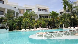 Un espace piscine avec des chaises longues et des palmiers.