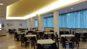 A spacious dining area with multiple tables and chairs, large windows with blue curtains, and a modern ceiling design. - Hotel Senio (Riolo Terme)