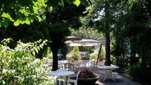 An outdoor patio area with round tables and chairs, surrounded by trees and covered by umbrellas. - Hotel Senio (Riolo Terme)