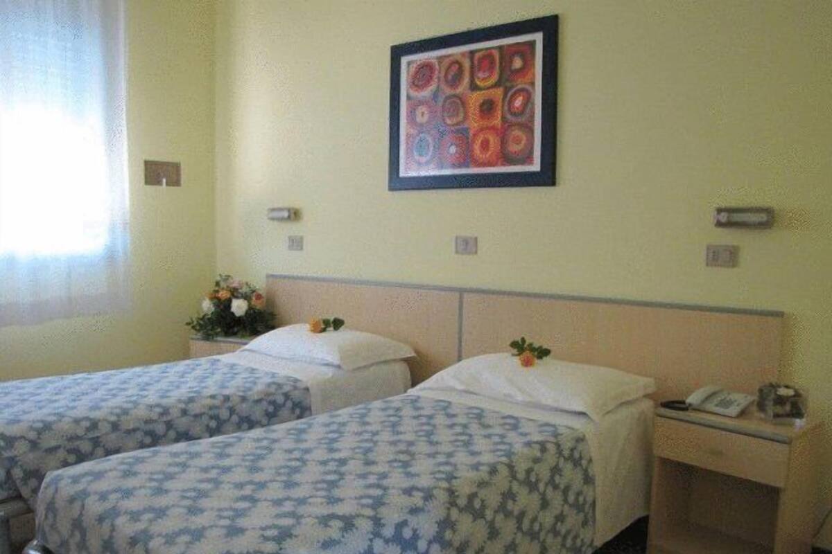 Una habitación de hotel con dos camas individuales, una mesita de noche pequeña con un teléfono y una obra de arte enmarcada en la pared.