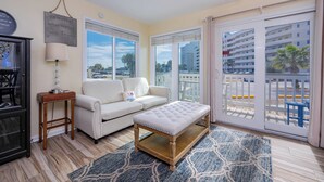 A living room with a white sofa, a wooden bench, a lamp, and a view of a balcony with a railing.