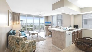 A modern living room with a sofa, chairs, a TV, a balcony with a view, and a kitchen area.