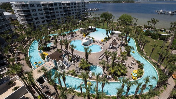 A large, multi-level hotel with a central swimming pool surrounded by palm trees and sun loungers.