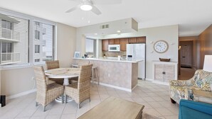 A modern kitchen with a central island, a dining area with wicker chairs, and a living room with a sofa and a coffee table.