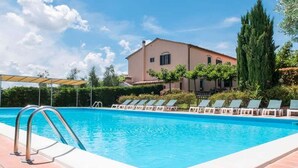 En swimmingpool med solstolar, en pergola och en byggnad med ett tak täckt av tegelpannor.