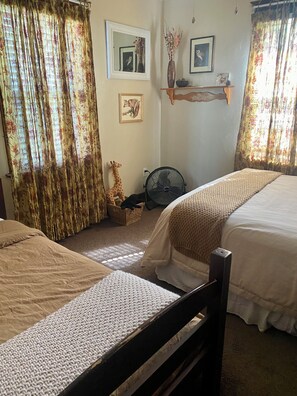 Een kamer met twee bedden, een ventilator, een plank met decoratieve objecten, en een girafbeeldje.
