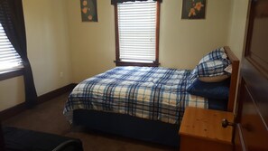 A bedroom with a bed, a nightstand, a dresser, and a window with blinds.