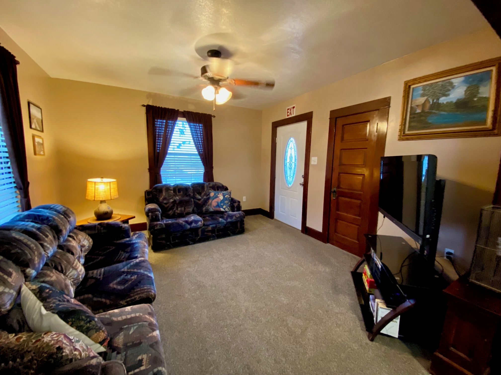 A living room with a ceiling fan, a couch, a television, and an exit door.