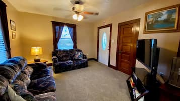 A living room with a ceiling fan, a couch, a television, and an exit door.