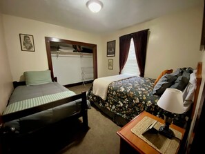 Une chambre avec deux lits, une armoire, une table de chevet avec une lampe et une fenêtre avec des rideaux.
